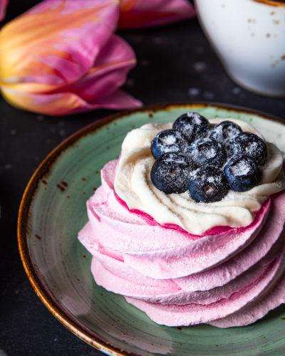Pavlova cake with blueberries on a plate close-up, tea and pink tulips vertical photo. High quality photo