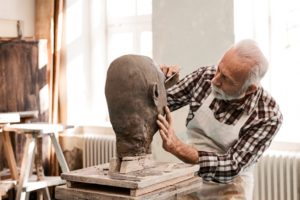 senior-man-making-statue-of-clay-shaping-a-face-with-work-tool-picture-id1227371990